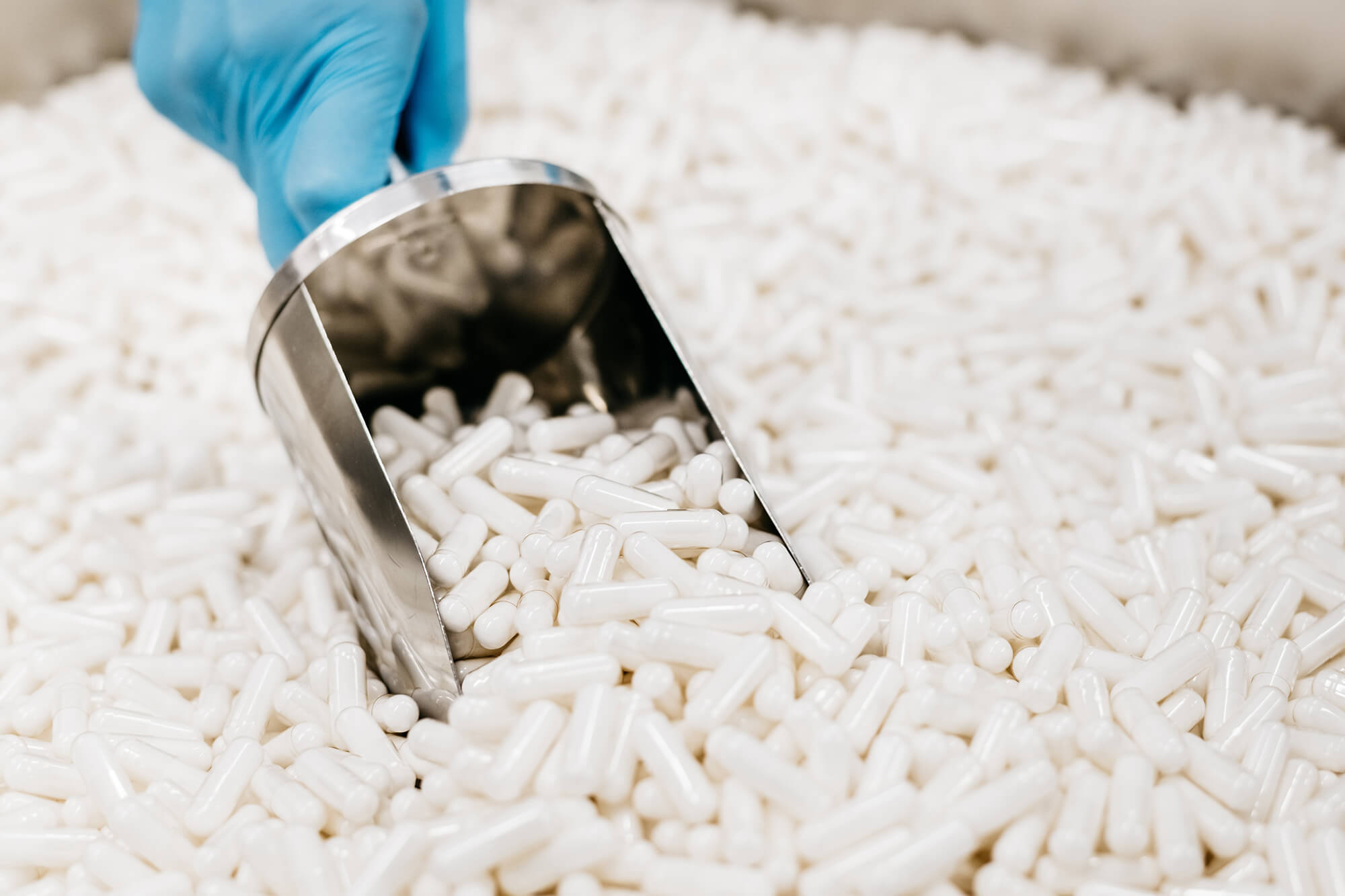 A person is scooping white pills out of a container.