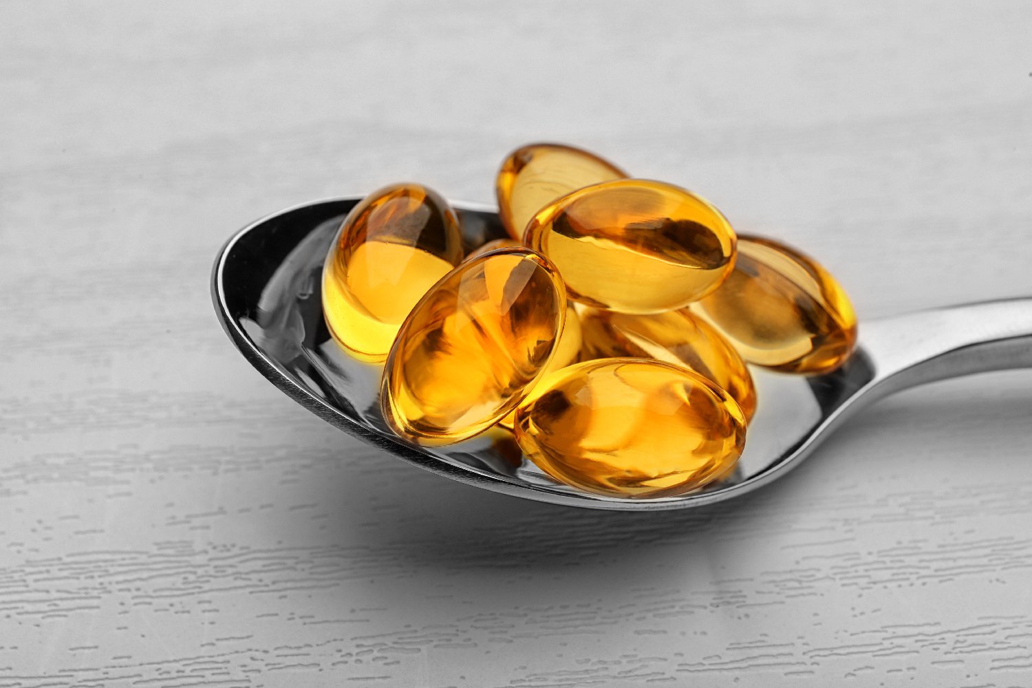 A spoon full of fish oil capsules on a table.