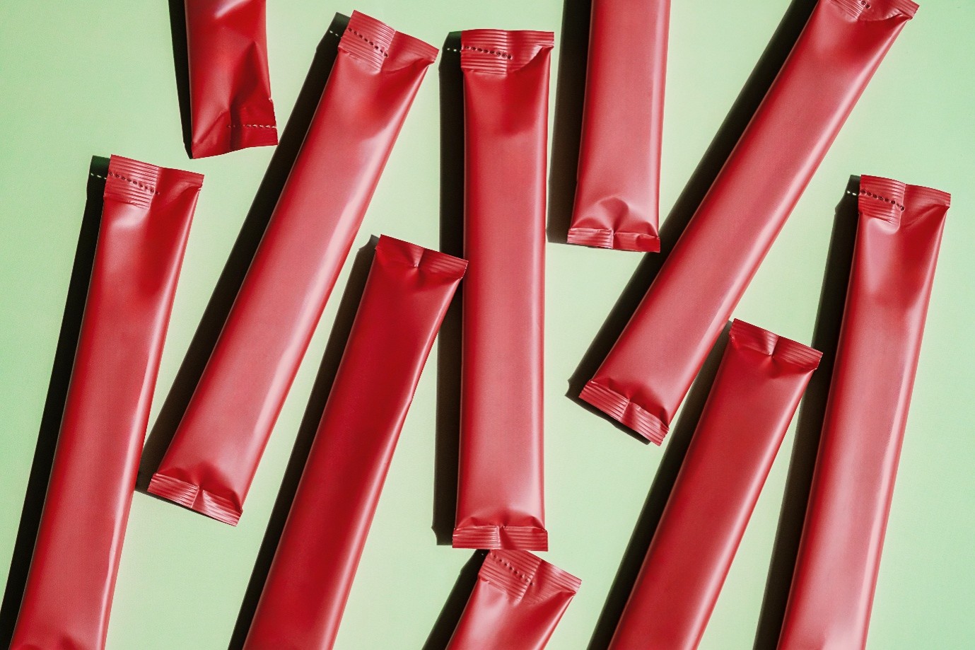 Several red, rectangular, individually wrapped packets are arranged in a scattered pattern on a light green surface.