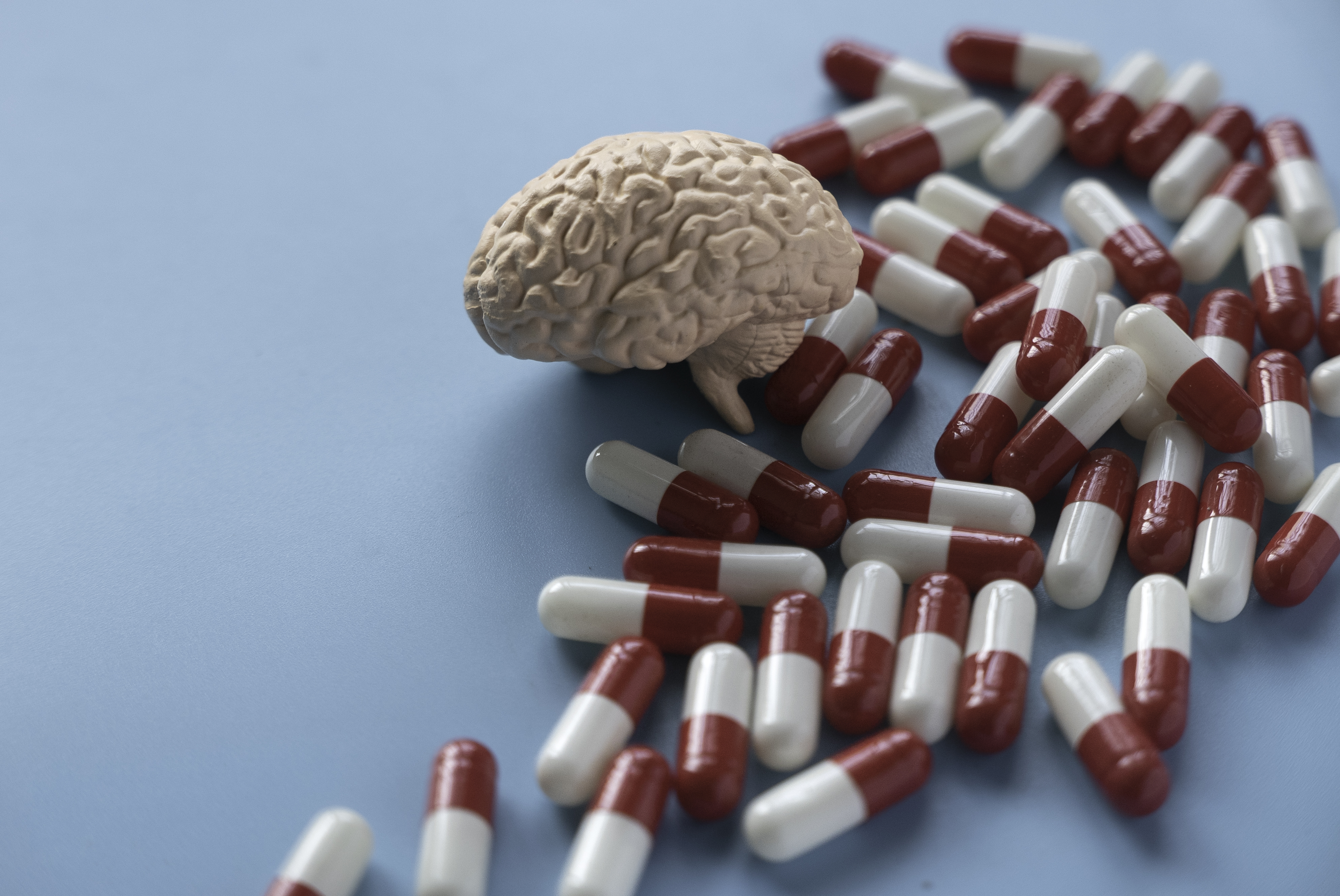 A small model of a human brain resting on a pile of red and white capsule pills.