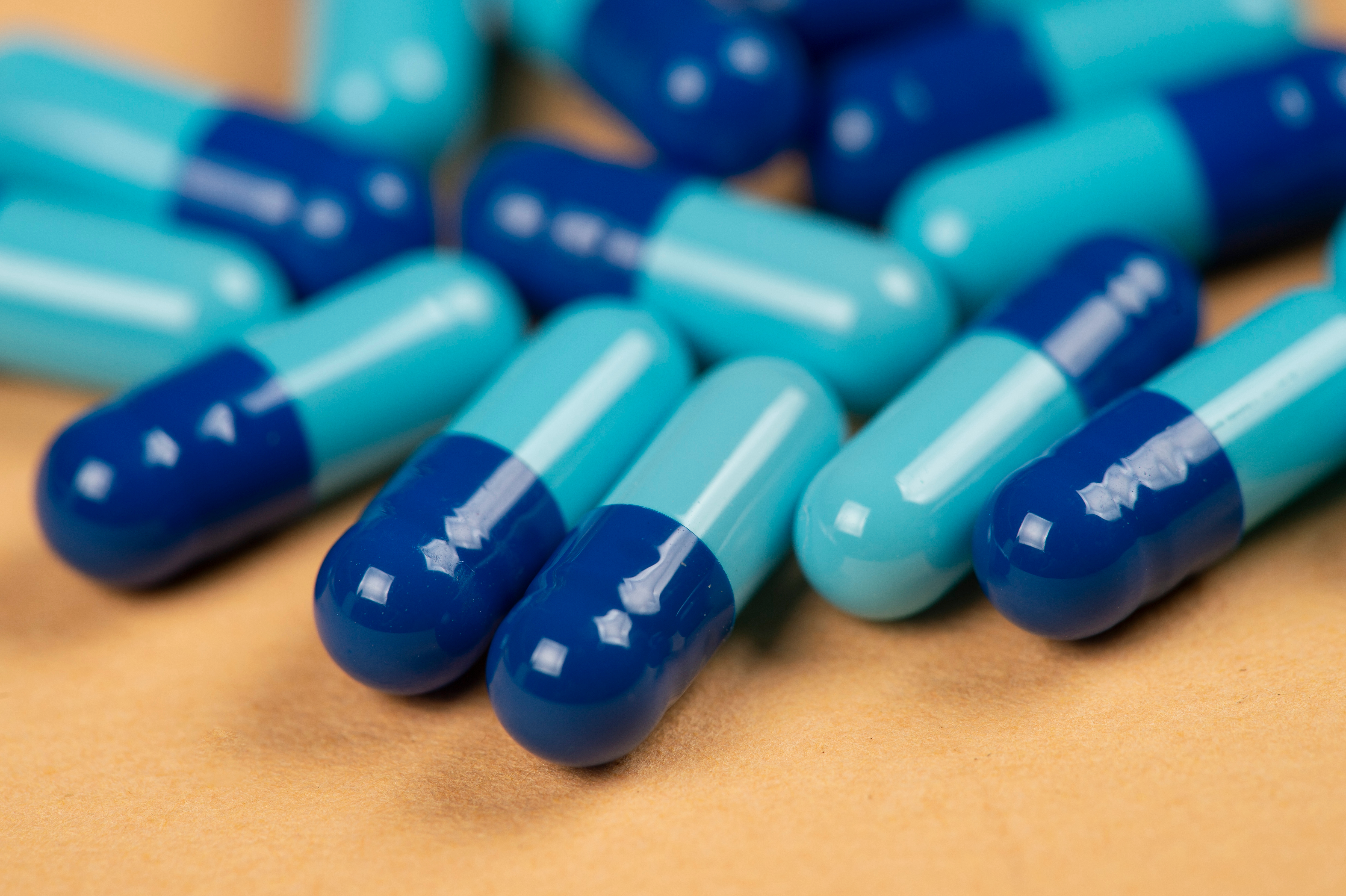 A pile of two-toned blue and teal capsules on a tan surface.