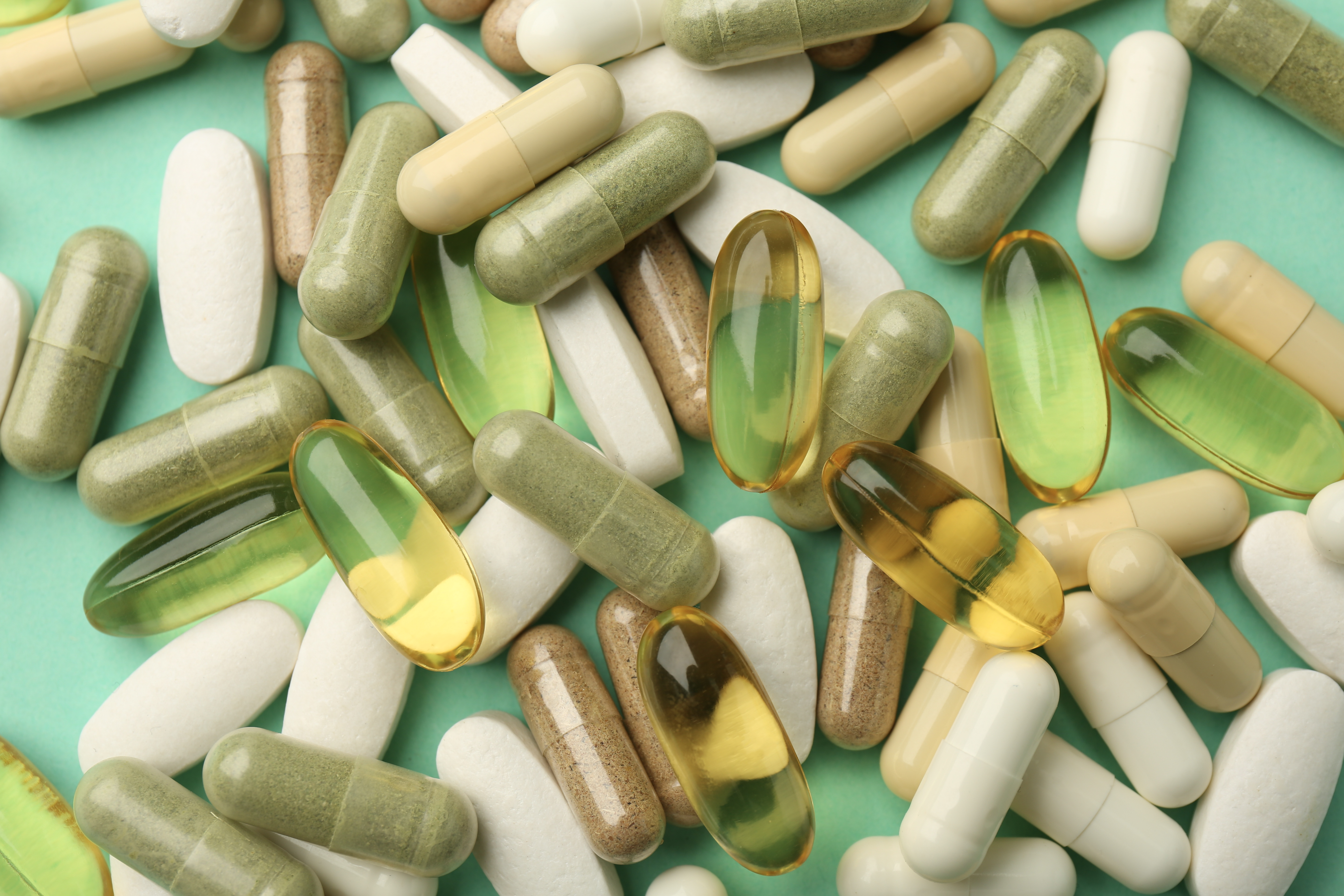 A collection of various white, green, brown, and translucent yellow supplement capsules scattered on a green surface.